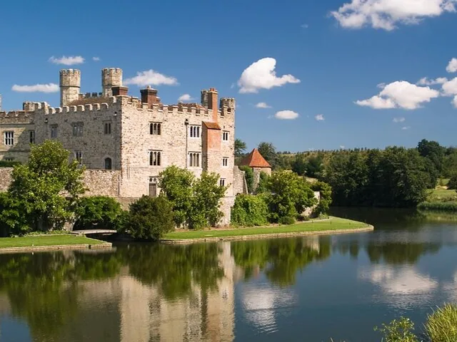Stone castle reflected in tranquil water under partly cloudy blue sky