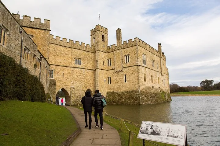 Two people walking towards a large stone castle entrance by water