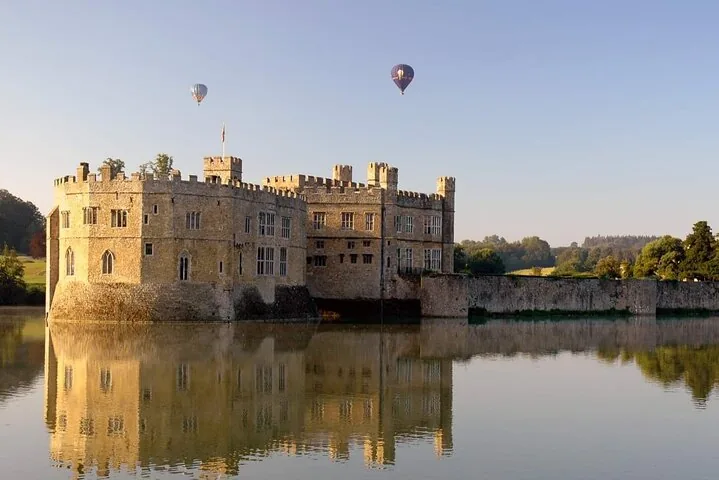 Castle surrounded by water with two hot air balloons in sky