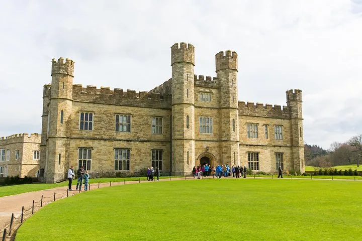 Tourists standing outside a large stone castle with a grassy lawn