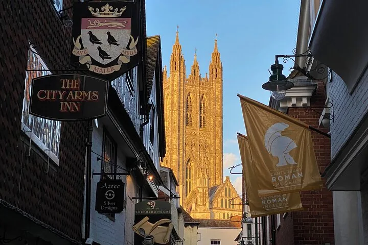 Narrow street view towards Canterbury Cathedral with hanging shop signs and flags